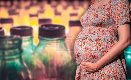Photo for Close-up of a pregnant belly with a blurred plastic bottles on the background. Low levels of microplastics and BPA may be harmful to the normal development of babies and infants - Royalty Free Image