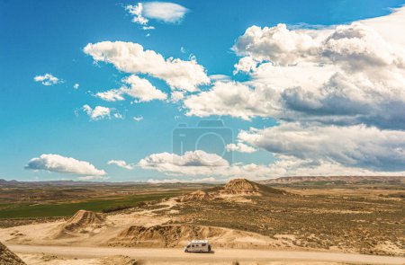 A captivating image capturing a camper van journeying through the breathtaking semidesert landscape of Bardenas Reales in Spain. The vast expanse of the natural park is highlighted by eroded