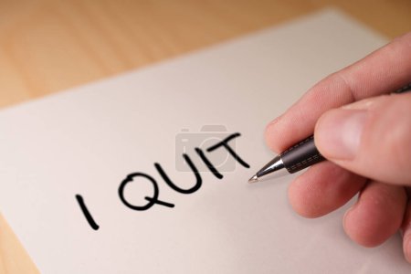 Close-up of a hand writing I Quit on a piece of paper with a pen, symbolizing resignation, quitting a job, ending a commitment or the great resignation, decision making to quit job, resign from paid