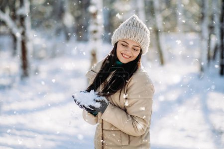 Photo for Portrait of a beautiful girl in winter clothes standing in a winter park on a sunny day and smiling. The winter vacation. Copy space. - Royalty Free Image
