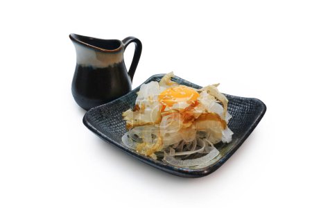 Téléchargez les photos : Katsuobushi sur des oignons tranchés servis avec des œufs crus sur le dessus, saupoudrés de graines de sésame, placés dans une assiette noire. - en image libre de droit