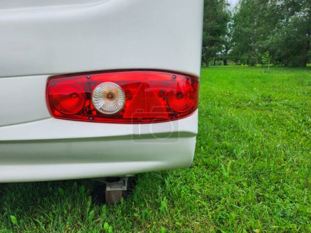 The image shows the red and white plastic tail light of a modern recreational vehicle. The light is in focus, while the green grassy background is blurred, creating a sense of depth and focus.