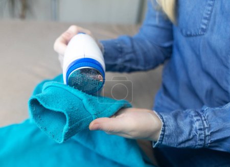 Photo for Machine for removing pellets. The girl uses a special device to remove lint from clothes. Restoration of old damaged clothes. - Royalty Free Image