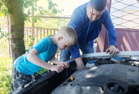 Photo for Timing belt break. Man and son near hood of car is looking for a malfunction due to which the engine does not work. Driver is holding a broken front belt in his hands. Shock due to irreparable damage. - Royalty Free Image