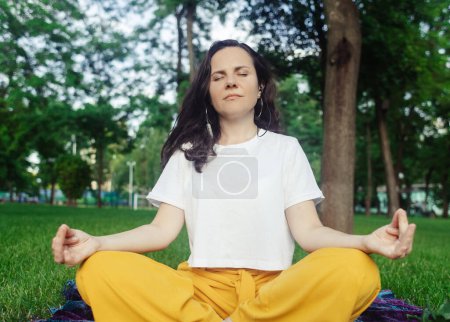 Photo for Solo yoga in park. Woman is engaged in meditation in the lotus position. Relaxation of the nervous system. Self-help in unloading the nervous system. Serenity and recovery - Royalty Free Image