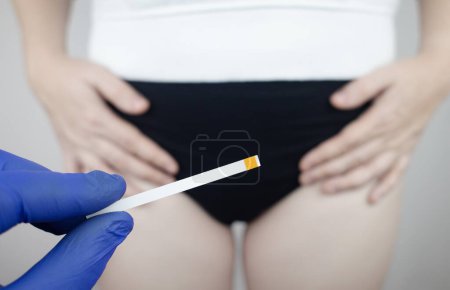 Photo for Bacterial Vaginosis. Vaginal pH. Girl shows sticks for measuring acid-base balance of genital organs. Self-diagnosis. Normal acidity level shown in colors and must be compared with the standard - Royalty Free Image