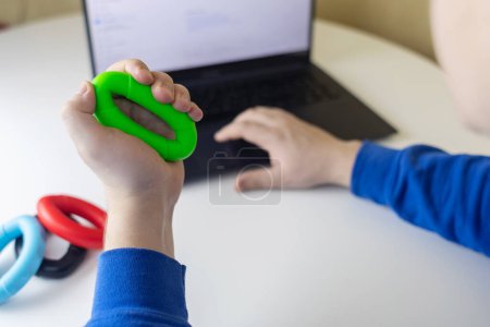 Pinza de mano. El hombre aprieta el expansor de goma mientras trabaja en su computadora portátil. Concepto de combinar la actividad útil con el trabajo necesario. Entrenamiento de músculos de mano y brazo. Mini aparato de entrenamiento multicolor