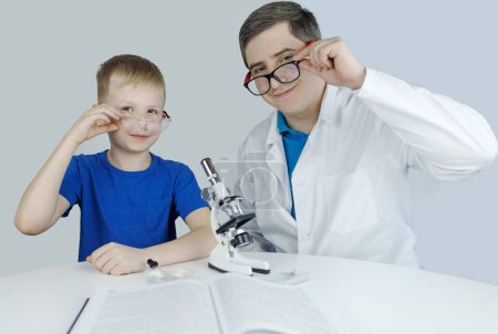Photo for Child chemist. Teacher shows a visual experiment. A science mentor teaches an experimental approach. Microscope, petri dish, pipettes, books. Practical work in chemistry or physics. Laboratory work - Royalty Free Image