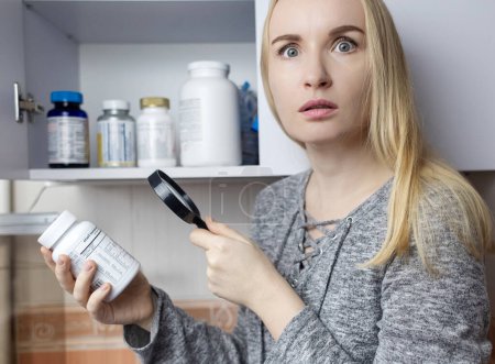 Girl studies dietary supplements. Reading the instructions on a bottle of vitamin complex. Nutritional supplement for hair loss and  weakened immunity. Self-prescription of drugs and harm to health