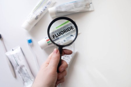 Gefährlicher Zahnpasta-Wirkstoff Fluorid. Kontrolle der Zusammensetzung von Zahnpasta mit einer Lupe vor dem Hintergrund vieler Tuben