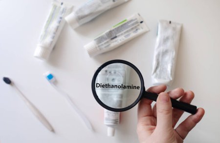 Dangerous toothpaste ingredient diethanolamine. Checking the composition of toothpaste with a magnifying glass against the background of many tubes
