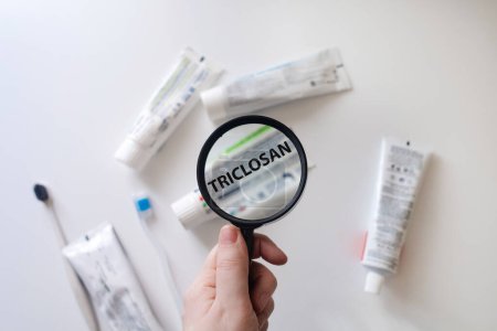 Dangerous toothpaste ingredient triclosan. Checking the composition of toothpaste with a magnifying glass against the background of many tubes