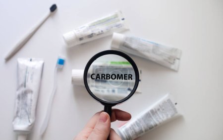 Dangerous toothpaste ingredient carbomer. Checking the composition of toothpaste with a magnifying glass against the background of many tubes