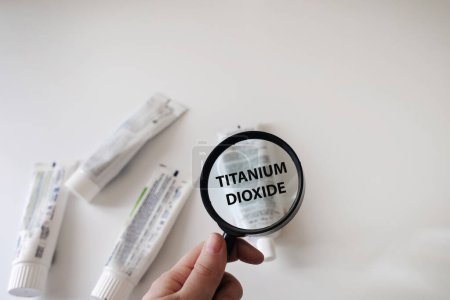 Dangerous toothpaste ingredient titanium dioxide. Checking the composition of toothpaste with a magnifying glass against the background of many tubes