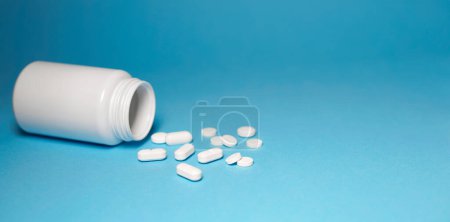 Photo for Medicine pills medical and pharmaceutical concept with white tablets bottle and pills scattered on blue background horizontal banner with copy space. - Royalty Free Image