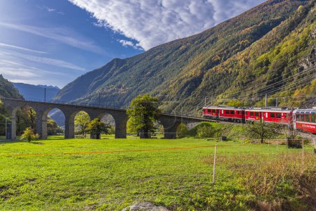 Foto de BRUSIO, SUIZA - 28 DE OCTUBRE DE 2022: Bernina Express de la línea ferroviaria Rhaetian en el viaducto espiral de Brusio en un día de otoño en la Suiza italiana - Imagen libre de derechos