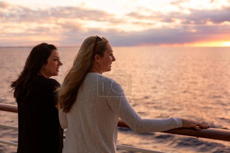 Téléchargez les photos : Deux jolies femmes d'âge moyen profitant de la vue sur le coucher du soleil depuis le pont d'un bateau de croisière pendant leurs vacances ensemble dans les Caraïbes - en image libre de droit
