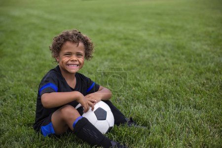 Photo for Young African American soccer player sitting on a grass field expressionless before a soccer game - Royalty Free Image