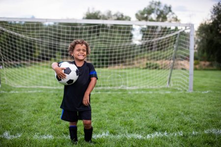 Photo for Young African American soccer standing in front of a soccer goal smiling before a soccer game on a large grass field. - Royalty Free Image