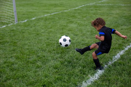 Foto de Joven jugador de fútbol afroamericano pateando la pelota en el gol durante un partido de fútbol en un campo de hierba grande - Imagen libre de derechos