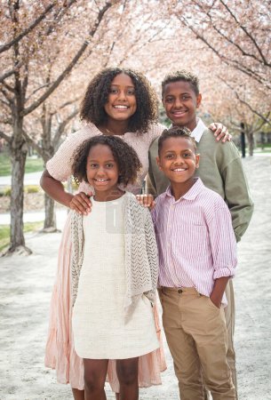 Photo for Portrait of a beautiful group of diverse children standing in a row of cherry blossom trees. Smiling African American siblings posing together. Diverse Family concept - Royalty Free Image