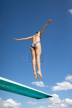 Foto de Vista desde abajo. Mujer en forma saltando alto de un trampolín en la piscina. Imagen abstracta con cielo azul y nubes en el fondo. Un montón de espacio de copia. - Imagen libre de derechos