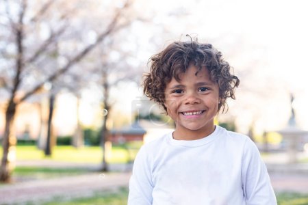 Foto de Sonriendo feliz Mixed-race pequeño niño de pie en el parque y mirando a la cámara - Imagen libre de derechos