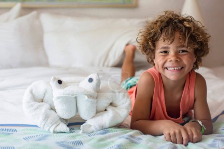 Foto de Sonriente adorable mixto-raza pequeño niño en cama con toalla juguete - Imagen libre de derechos