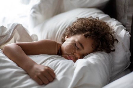 Foto de Adorable mixto-raza pequeño niño durmiendo en cama - Imagen libre de derechos