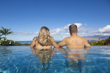 Téléchargez les photos : Vue arrière d'un beau couple dans une piscine à débordement donnant sur un paysage d'îles tropicales à Hawaï. Vue sur l'océan sur une belle île. Voyage, bonheur, luxe, concept de vacances d'été. - en image libre de droit