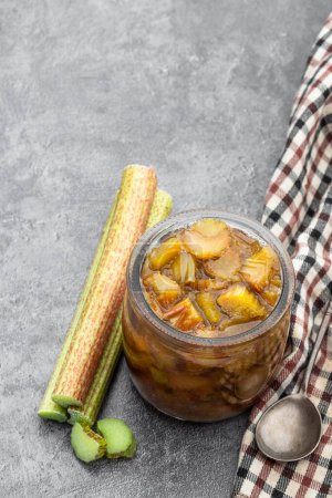 Homemade  rhubarb jam in jar with raw stalk rhubarb on gray background 