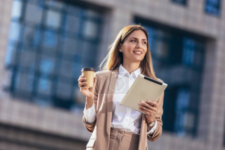 Téléchargez les photos : Femme d'affaires attrayante utilisant une tablette numérique tout en se tenant devant le bâtiment d'affaires. - en image libre de droit
