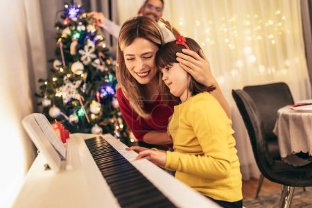 Foto de Padres jóvenes disfrutando de la música que su hija toca en el piano durante la Navidad - Imagen libre de derechos