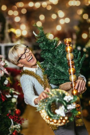 Foto de Mujer mayor en el mercado de Navidad comprando árboles, juguetes de decoración y pelotas. Concepto de compras de Navidad y Año Nuevo. - Imagen libre de derechos