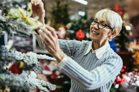 Foto de Mujer mayor en el Mercado de Navidad comprando juguetes decorativos y pelotas. Concepto de compras de Navidad y Año Nuevo. - Imagen libre de derechos