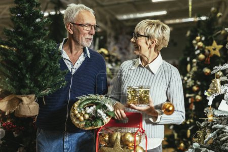 Téléchargez les photos : Couple aîné au marché de Noël acheter arbre, jouets de décoration et balles. Concept de Noël et du Nouvel An shopping. - en image libre de droit