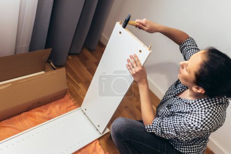 Photo for Woman in casual clothing sitting on the floor of her apartment and assembling furniture - Royalty Free Image