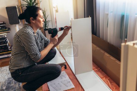 Photo for Woman in casual clothing sitting on the floor of her apartment and assembling furniture - Royalty Free Image
