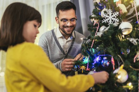 Téléchargez les photos : Père aimant célèbre Noël avec sa fille près du magnifique arbre de Noël - en image libre de droit