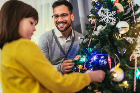 Téléchargez les photos : Père aimant célèbre Noël avec sa fille près du magnifique arbre de Noël - en image libre de droit