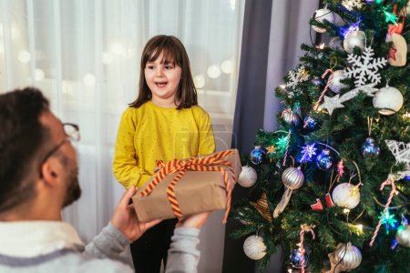 Foto de Padre cariñoso celebra la Navidad con su hija junto al hermoso árbol de Navidad - Imagen libre de derechos