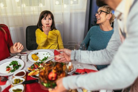 Foto fängt die Wärme und Freude eines Weihnachtsessen mit einer geliebten Großmutter, Mutter, Vater und Tochter ein. Die Familie ist um den festlichen Tisch versammelt, lächelt und lacht, während sie ein traditionelles Truthahnfest, Füllung und all das andere genießen.