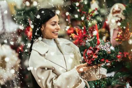 Téléchargez les photos : Jeune femme sélectionnant des décorations de Noël dans la boutique de produits décoratifs. La fille achète des décorations de Noël. - en image libre de droit