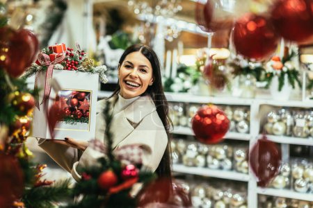 Foto de Mujer joven seleccionando decoraciones navideñas en la tienda de artículos decorativos. La chica compra decoraciones navideñas. - Imagen libre de derechos
