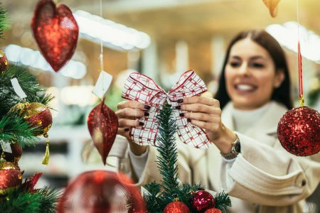 Foto de Mujer joven seleccionando decoraciones navideñas en la tienda de artículos decorativos. La chica compra decoraciones navideñas. - Imagen libre de derechos