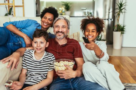 Téléchargez les photos : Jeune famille regardant la télévision ensemble à la maison et s'amusant ensemble
. - en image libre de droit