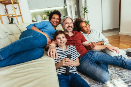Téléchargez les photos : Jeune famille regardant la télévision ensemble à la maison et s'amusant ensemble
. - en image libre de droit