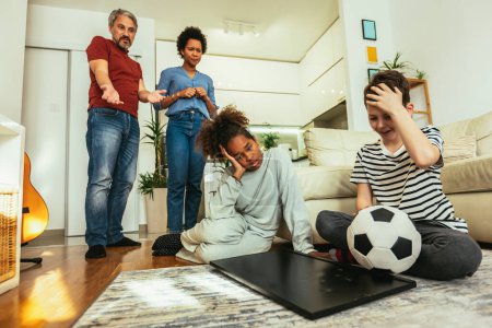 Foto de Niños tristes de pie frente a un televisor con la pantalla rota sosteniendo una pelota. Concepto de seguro doméstico. - Imagen libre de derechos