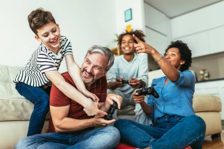 Téléchargez les photos : Smiling family enjoying time together at home sitting on sofa in living room and playing video games. - en image libre de droit