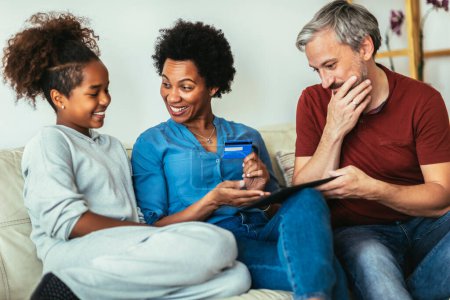 Téléchargez les photos : Famille utilisant la tablette numérique et la carte de crédit à la maison pour les achats en ligne. - en image libre de droit